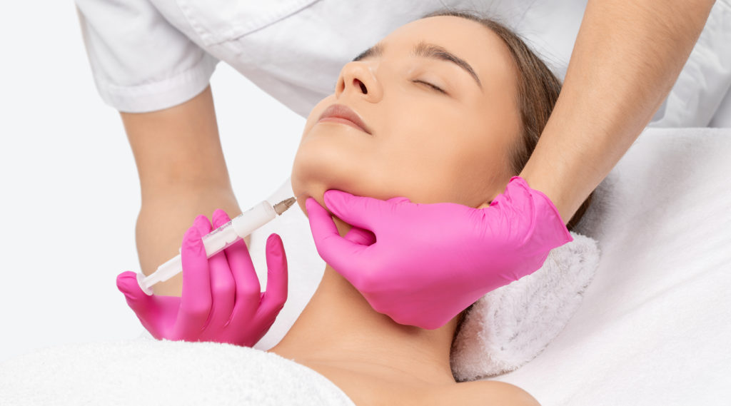 Cosmetologist makes lipolytic injections to burn fat on the chin, cheeks and neck of a woman against double chin. Female aesthetic cosmetology in a beauty salon. Cosmetology concept. | Skin Parlour